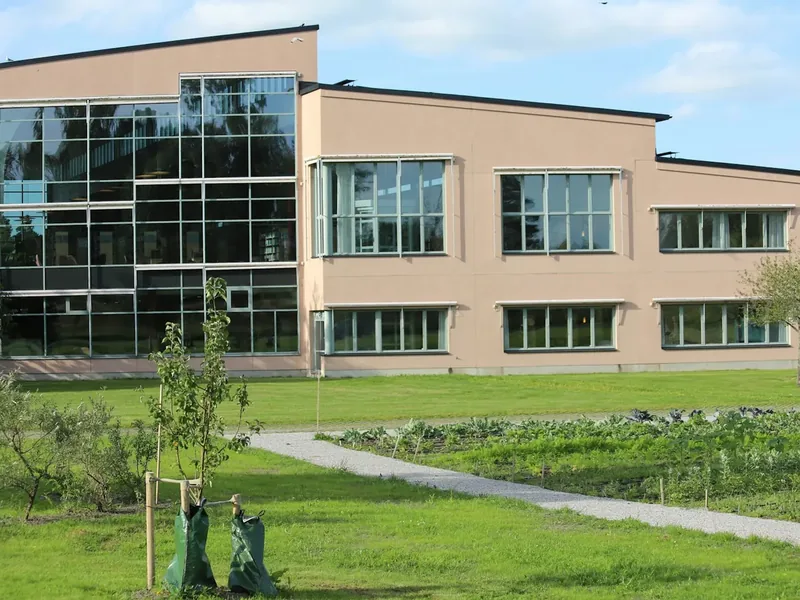 Modern school building with a glass stair tower, set behind a lawn and walking path