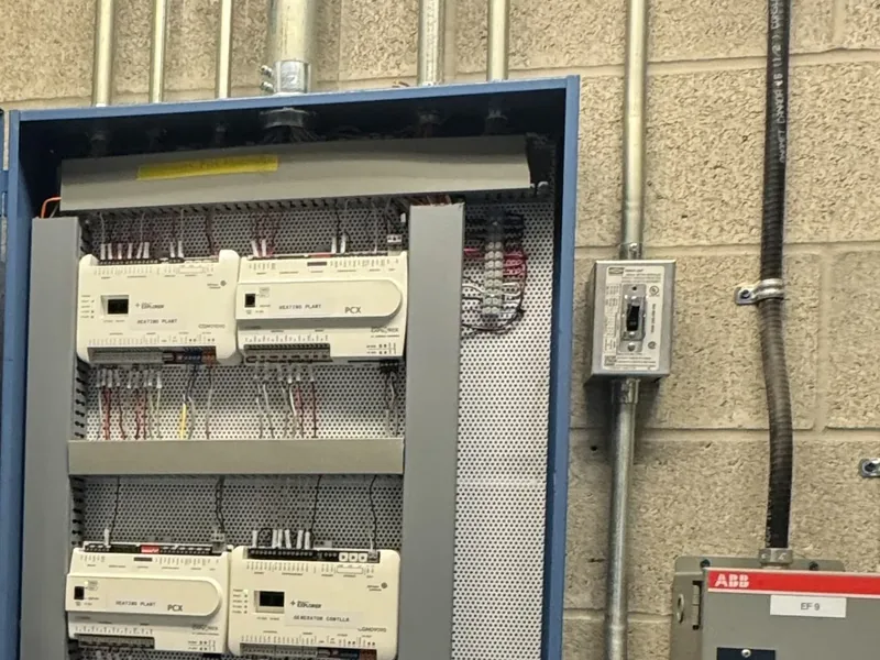 Building automation control panel with heating plant controllers terminated, next to conduit runs in a mechanical room